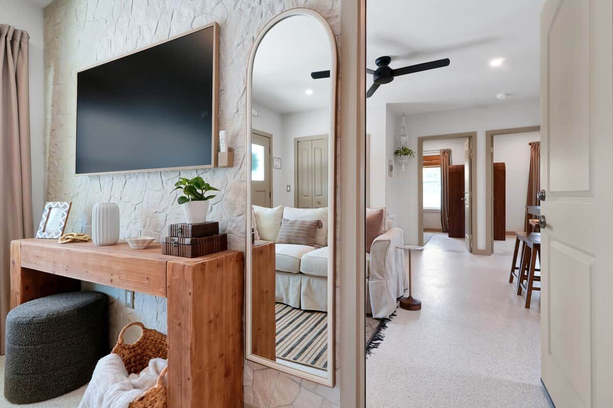 A modern interior with a stone wall, a flat-screen TV, a wooden console table, a mirror, and a hallway leading to a bedroom.