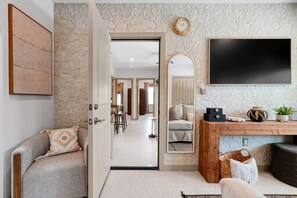 A room with a stone wall, a flat-screen TV, a wooden console table, and a door leading to another space. - Casa Blanca Cocoa Beach, 2 minutes to the beach with saltwater pool! (Cocoa Beach)