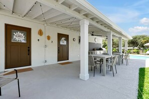 A covered outdoor patio with tables and chairs, a barbecue grill, and a pool in the background. - Casa Blanca Cocoa Beach, 2 minutes to the beach with saltwater pool! (Cocoa Beach)