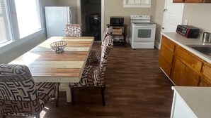 Una cocina con mesa de comedor, sillas, microondas, horno, armarios de madera y una ventana con persianas.