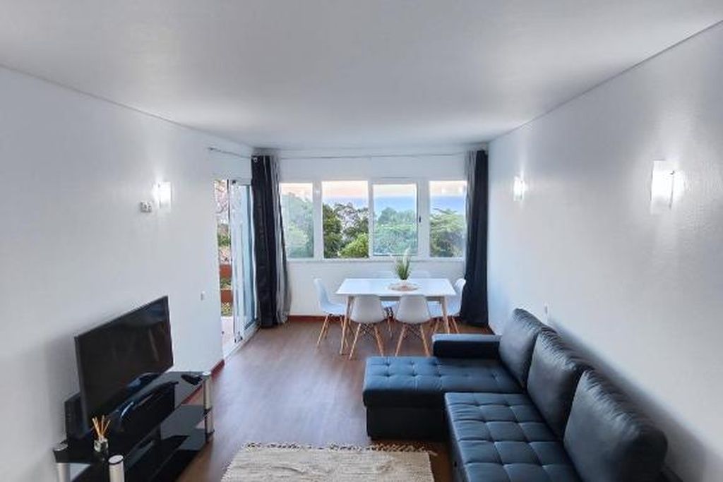 Un salon moderne avec un canapé noir, un téléviseur à écran plat et un coin repas comprenant une table et des chaises.