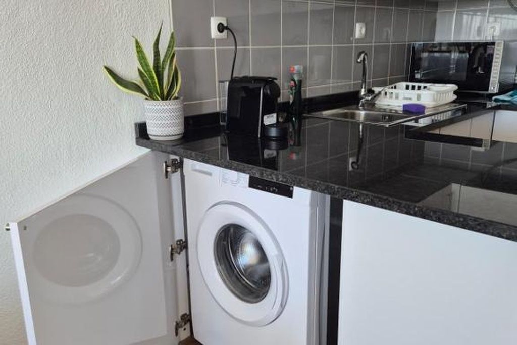 Cocina compacta con lavadora y secadora integradas, microondas y un lavamanos pequeño.
