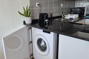Una cuina compacta amb rentadora i assecadora integrades, microones i un petit banyador.