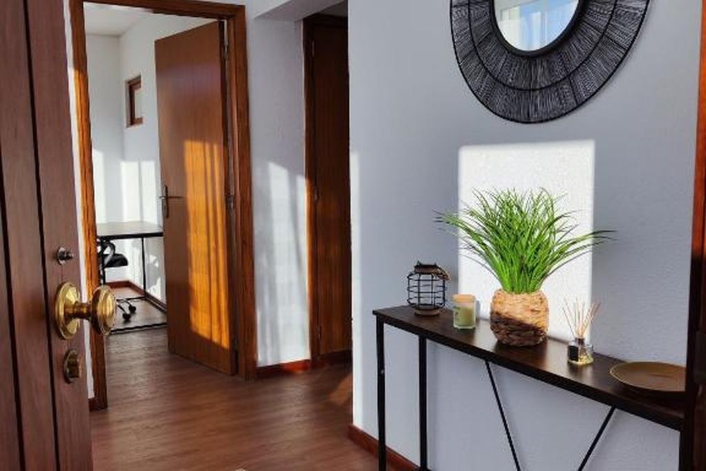 Un couloir avec une porte en bois, un miroir rond accroché au mur et une petite table sur laquelle se trouvent une plante et une bougie.