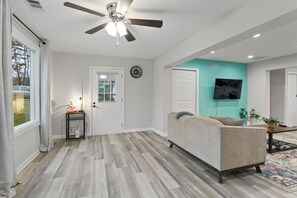 A modern living room with a ceiling fan, a sofa, a television, and a patterned rug.