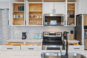 Une cuisine avec des meubles blancs, un four à micro-ondes en acier inoxydable, une cuisinière noire et une machine à café.