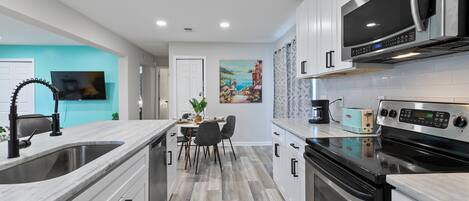 Una cocina moderna con armarios blancos, electrodomésticos de acero inoxidable y un comedor con mesa y sillas.