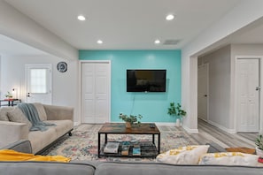 A living room with a sofa, coffee table, and a flat-screen TV mounted on the wall. - Cozy Decatur Oasis | 3BR + Yard | Emory & CDC (Decatur)