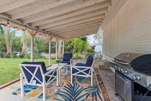 An outdoor patio with a grill, two chairs, and a table.