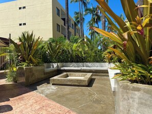 Una terrazza sul tetto con un'area salotto in cemento, immersa in piante tropicali rigogliose e palme.