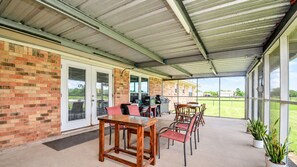 Un espace extérieur aménagé en patio, avec un mur en briques, des portes-fenêtres coulissantes, un coin barbecue et des sièges d’extérieur.