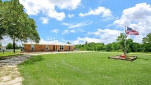 A brick building with a lawn and an American flag. - 5-Acre Ranch Retreat with Pool near Medical Center & NASA (Rosharon)