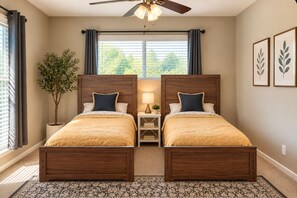 Une chambre à coucher avec deux lits en bois, un ventilateur de plafond, une fenêtre avec des rideaux, une table de chevet avec une lampe et une plante en pot.