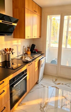 Une cuisine moderne avec des meubles en bois, un plan de travail noir, un four encastré et un lave-vaisselle.