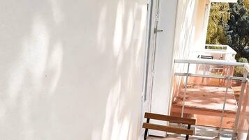 Un espace patio avec des tables et des bancs en bois, un mur blanc et une porte donnant sur un espace extérieur.