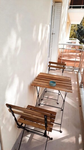 Un espace patio avec des tables et des bancs en bois, un mur blanc et une porte donnant sur un espace extérieur.