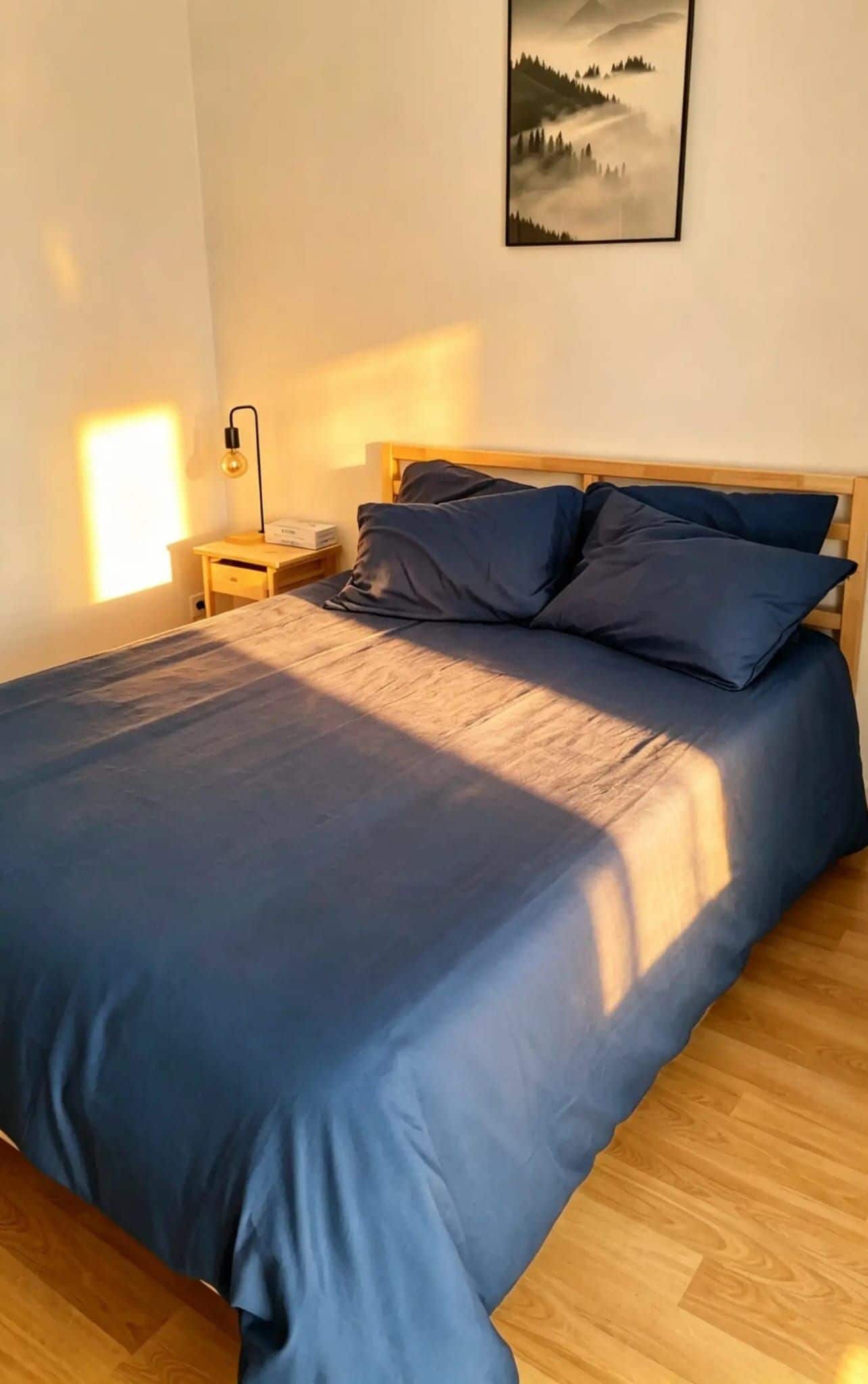 Ein Schlafzimmer mit einem Bett, einem Holzkopfteil, einem Nachttisch, einer Lampe und einem gerahmten Bild an der Wand.
