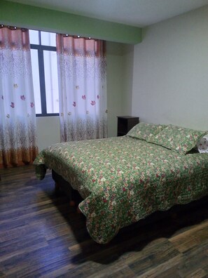 A bedroom with a bed, a window with curtains, and a wooden floor.