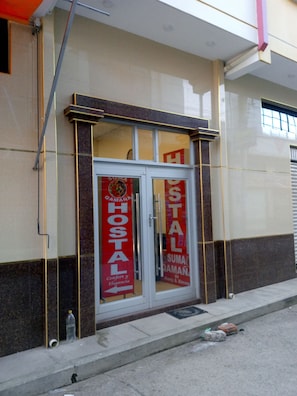 A hotel entrance with a glass door and two vertical banners advertising the hotel's name and services. - Hostal Suma Qamaña (Copacabana)