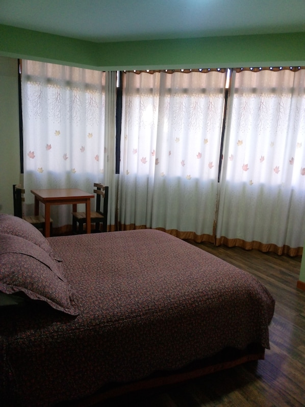 A room with a bed, a small table, and curtains with a leaf pattern.