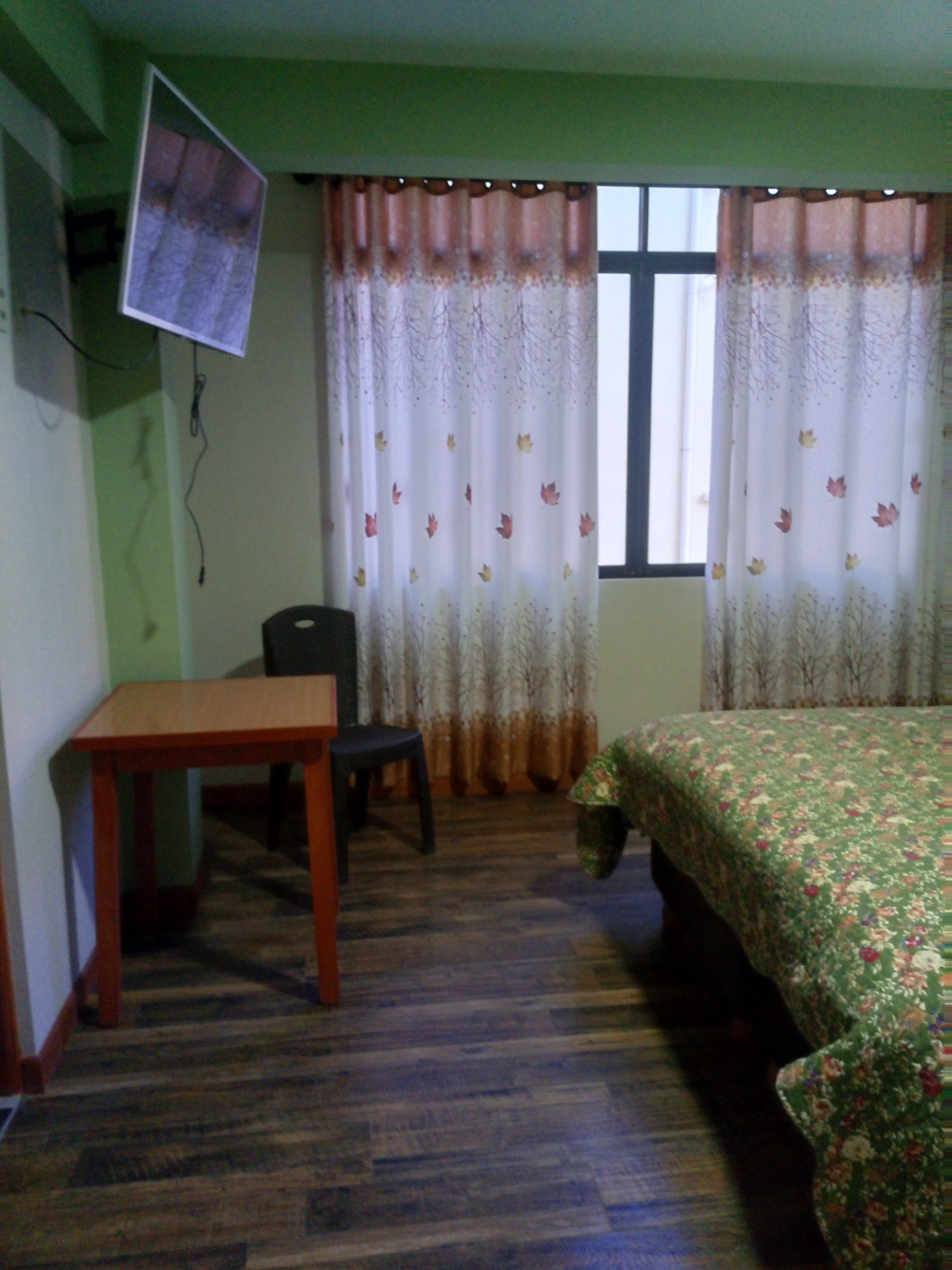 Una habitación con cama, escritorio, silla y televisor montado en la pared.