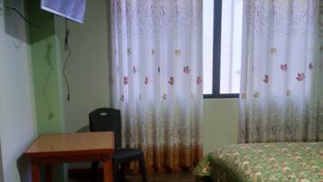Una habitación con cama, escritorio, silla y televisor montado en la pared.