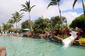 Une piscine aux eaux cristallines, avec un toboggan, des chaises longues et des palmiers.