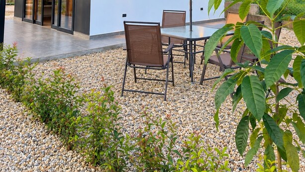 Un espace extérieur moderne aménagé avec une table et des chaises, un grand parasol et un sol recouvert de gravier.