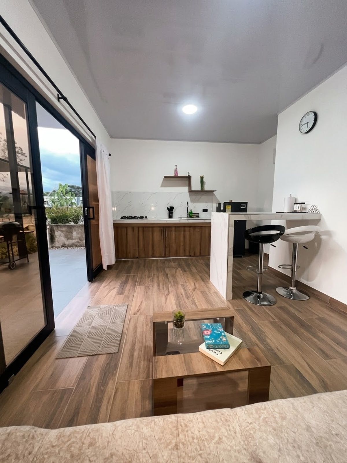Et moderne køkken med spiseområde, et sofabord med en bog og udsigt gennem en glasdør.