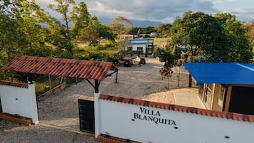 En lukket ejendom kaldet 'Villa Blanquita' med en grusvej, et overdækket parkeringsområde og udsigt over det omkringliggende landskab.