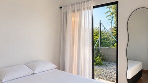 Une chambre moderne avec un grand lit, une porte-fenêtre coulissante donnant sur un espace extérieur et un miroir sur le mur.