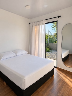 Een moderne slaapkamer met een groot bed, een schuifdeur naar buiten en een spiegel aan de muur.