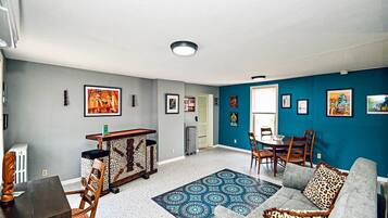 A living room with a sofa, a coffee table, a dining table with chairs, a patterned rug, and artwork on the walls.