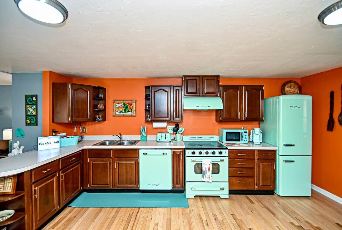 A kitchen with wooden cabinets, a teal refrigerator, and a vintage stove.