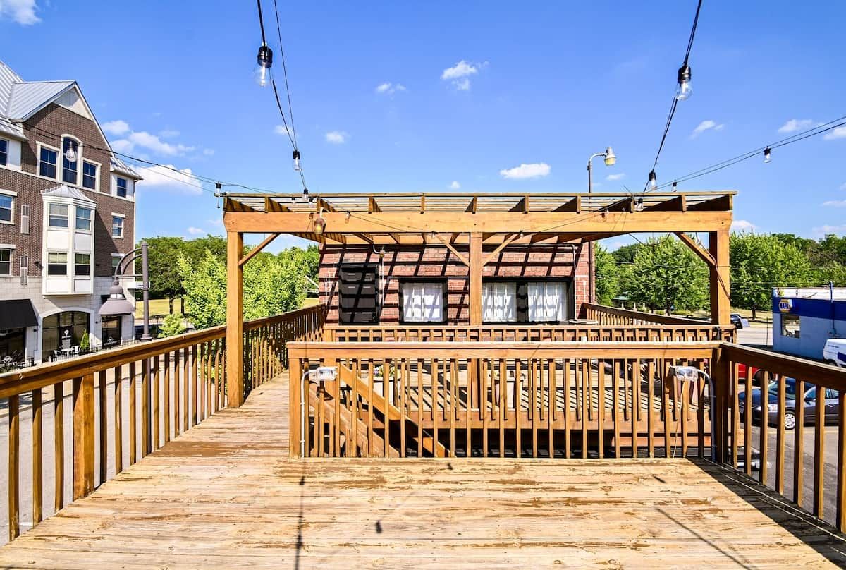 A wooden deck with a railing, a covered seating area, and a view of a brick building.