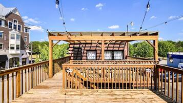 A wooden deck with a railing, a covered seating area, and a view of a brick building.