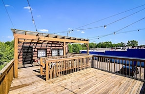 A wooden deck with a pergola structure, a small enclosed area with a door, and a view of a parking lot and buildings in the background.