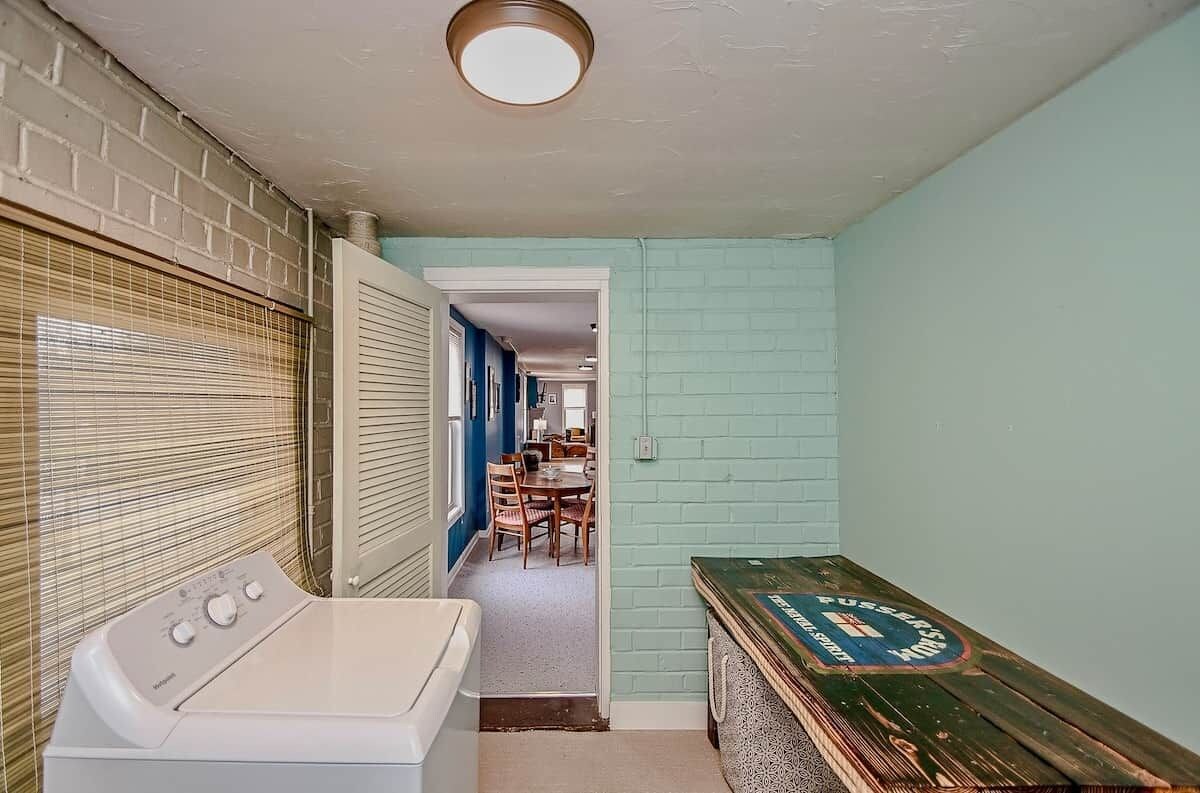 A laundry area with a washing machine, a drying rack, and a wooden bench with a vintage design.
