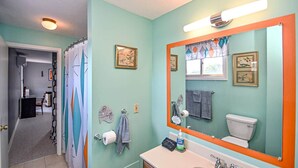 Un bagno con uno specchio grande, un WC e un lavandino. Si vedono asciugamani e una tenda da doccia.