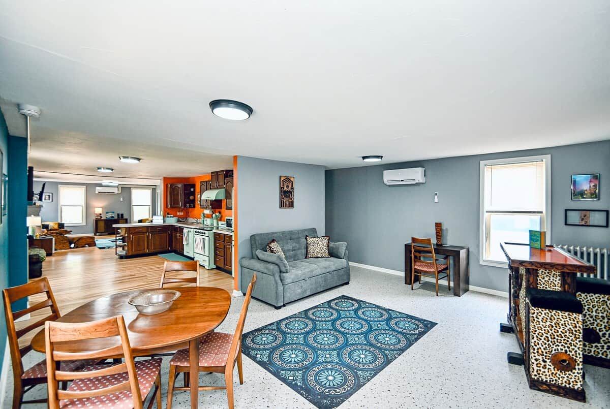 A modern living room with a dining area, grey walls, and a kitchen in the background.