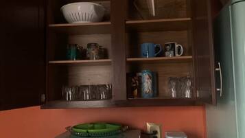 A kitchenette with a microwave, coffee maker, and a cabinet containing dishes and cups.