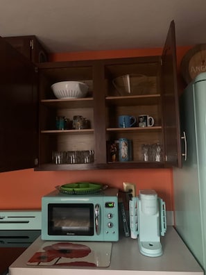 A kitchenette with a microwave, coffee maker, and a cabinet containing dishes and cups.