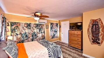 A bedroom with a bed, a ceiling fan, a dresser, and a wall with a tropical leaf pattern.
