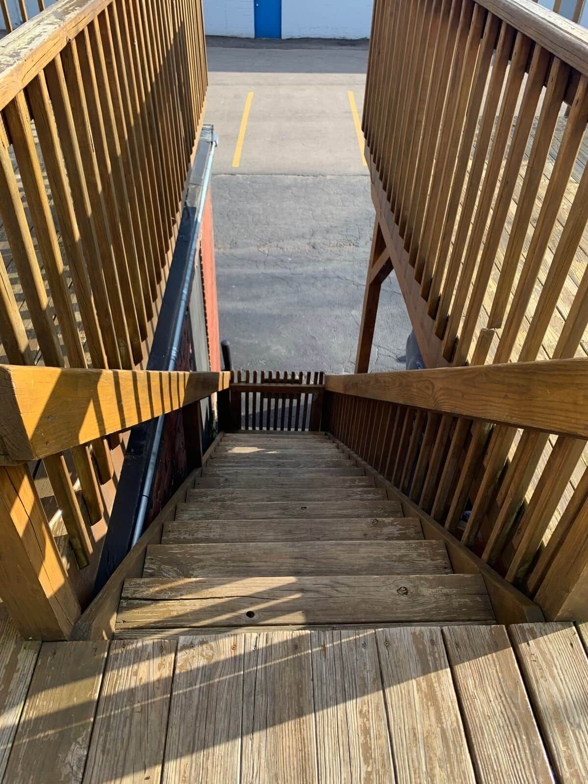 Un escalier en bois mène à une zone abritée, avec une porte bleue visible au fond.