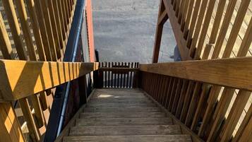 Un escalier en bois mène à une zone abritée, avec une porte bleue visible au fond.