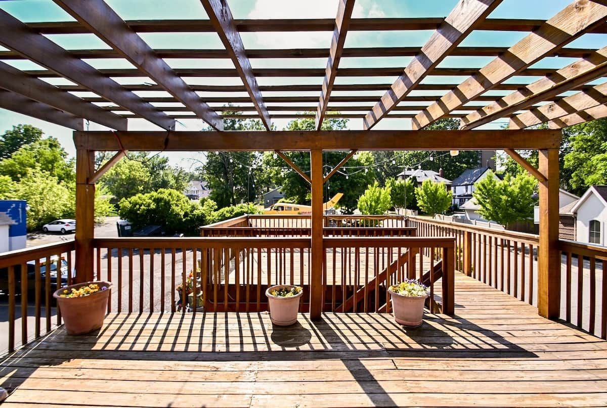 Une terrasse en bois agrémentée d’une pergola, de plantes en pot et offrant une vue sur un quartier résidentiel.