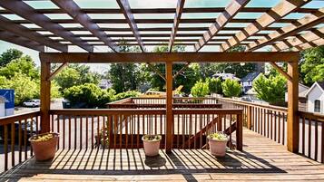 Une terrasse en bois agrémentée d’une pergola, de plantes en pot et offrant une vue sur un quartier résidentiel.
