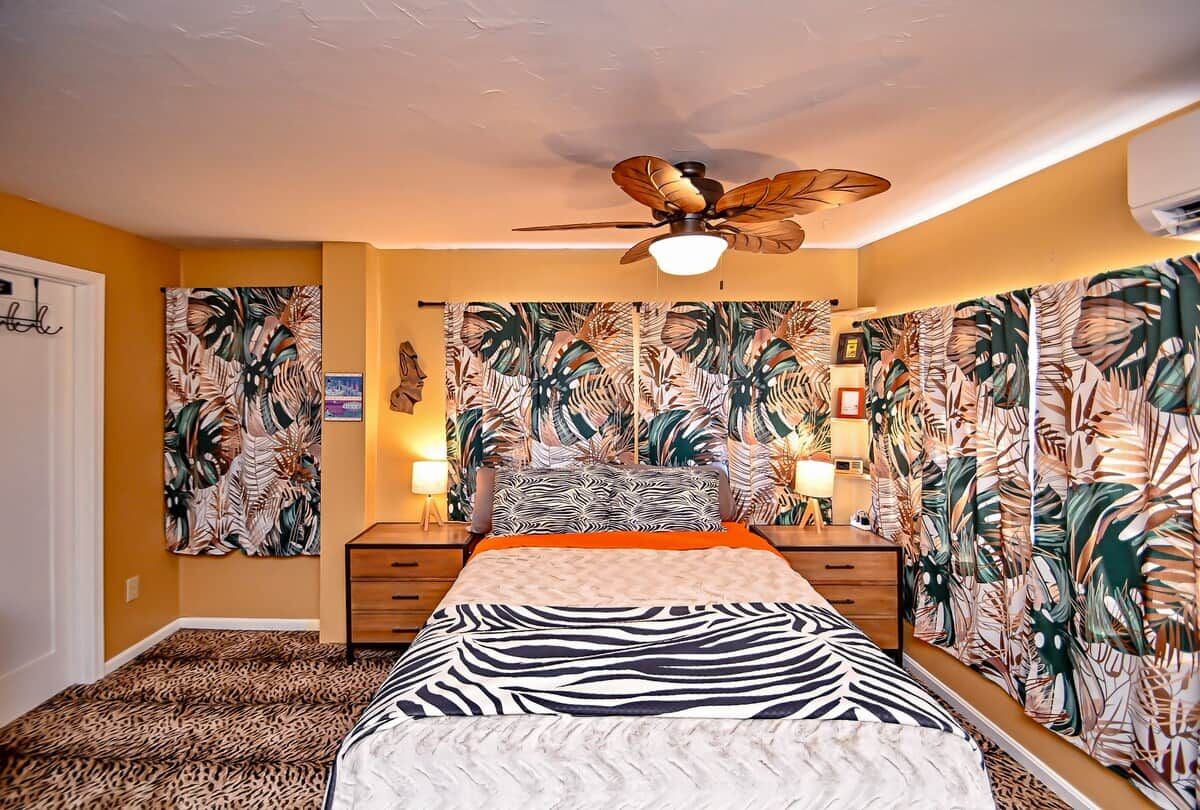 A bedroom with a bed, a ceiling fan, and tropical wallpaper.