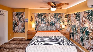 Una camera da letto con un letto, una ventola a soffitto e carta da parati tropicale.