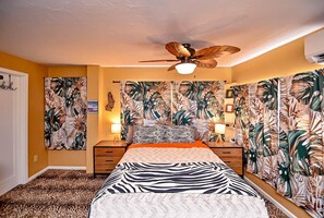 Een slaapkamer met een bed, een plafondventilator en tropische behang.